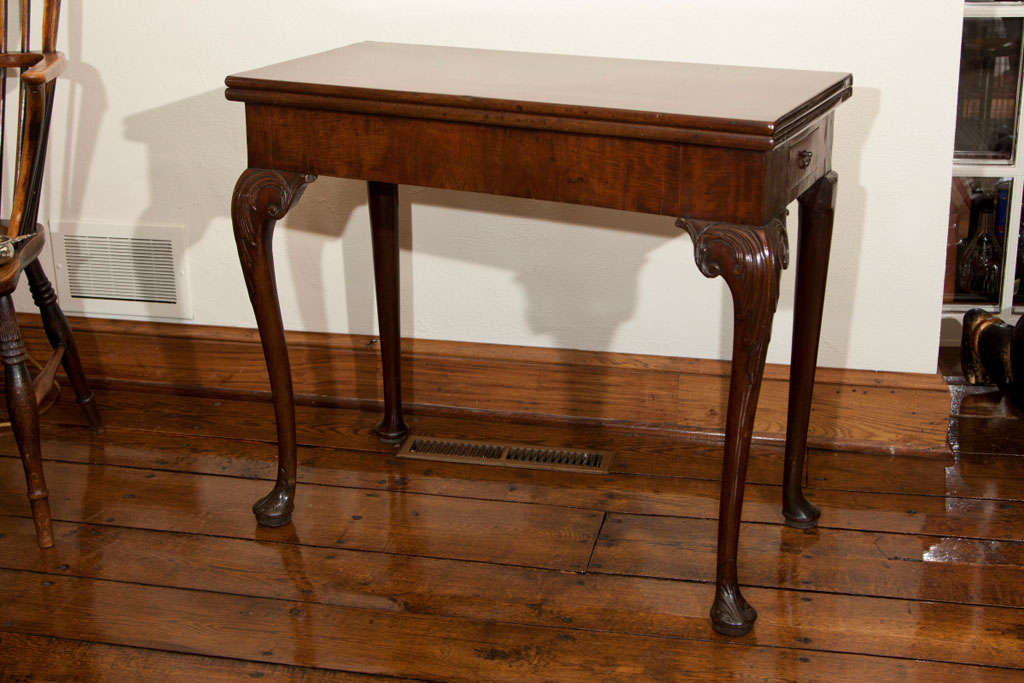 This handsome 18th century Irish flip top game table on cabriole legs features a swooping acanthus carving on the knees of the front legs which end in foliate carved pad feet. The back left leg swings to support the open top, itself covered in