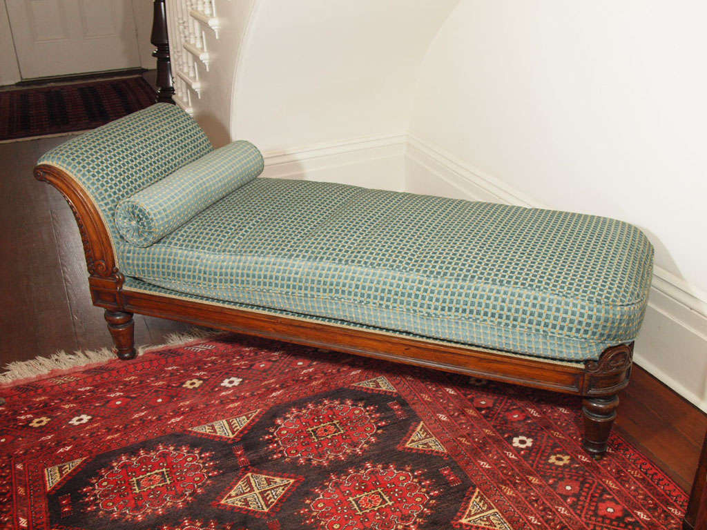 A second quarter of the 19th century English Georgian rosewood recamier having a backswept crest, faced with a C-scroll on one side, over a paneled seatrail and turned and tapering thick legs. It is fitted with a blue and gold geometric pattern
