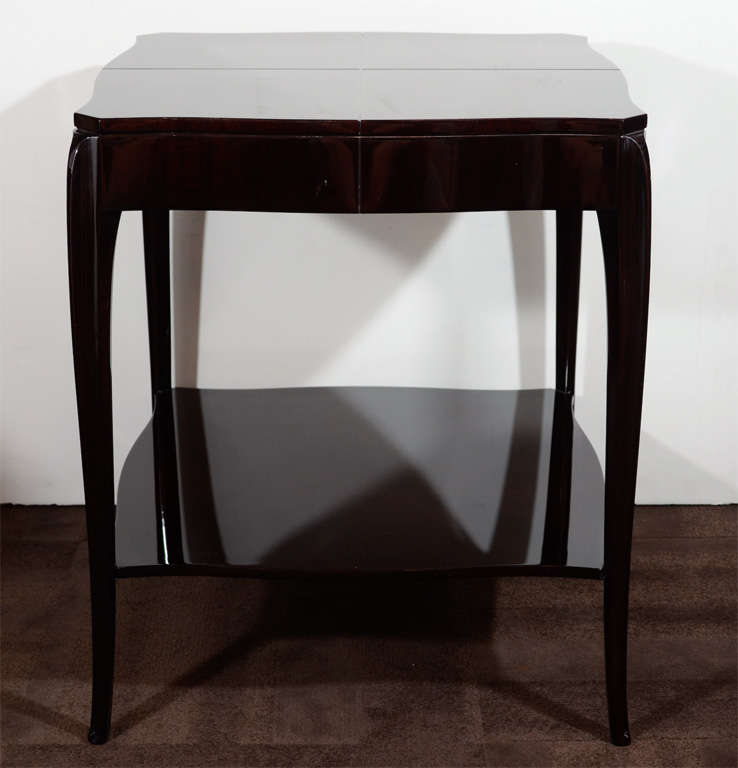 This sophisticated Art Deco/ Hollywood table was realized in the United States, circa 1945. It features a two tier Design in Ebonized Mahogany Wood with rectangular top with curved sides and Cabriole style legs. With its austere silhouette and clean