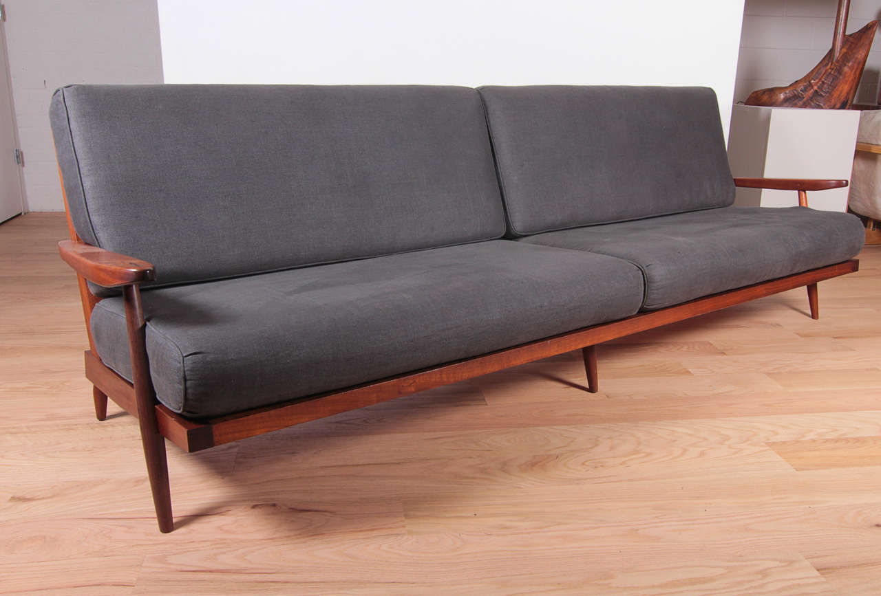 Sofa with arms in walnut, slatted back with loose cushions, with provenance.