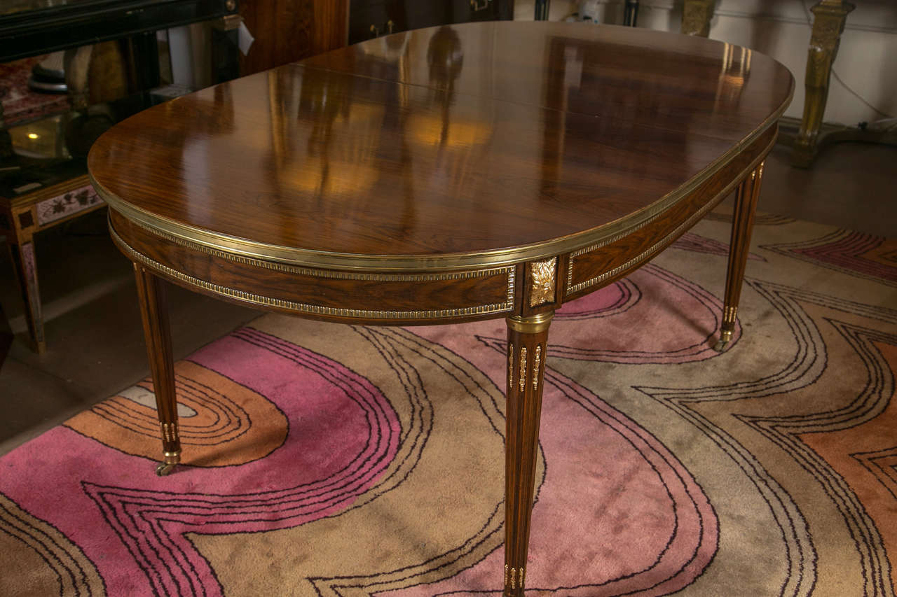 Simply the finest French Louis XVI style oval solid rosewood dining table. The circa 1940s beautiful rosewood oval top with bronze banding over a narrow frieze decorated with bronze pateras, raised on fluted tapering legs ending in castors on