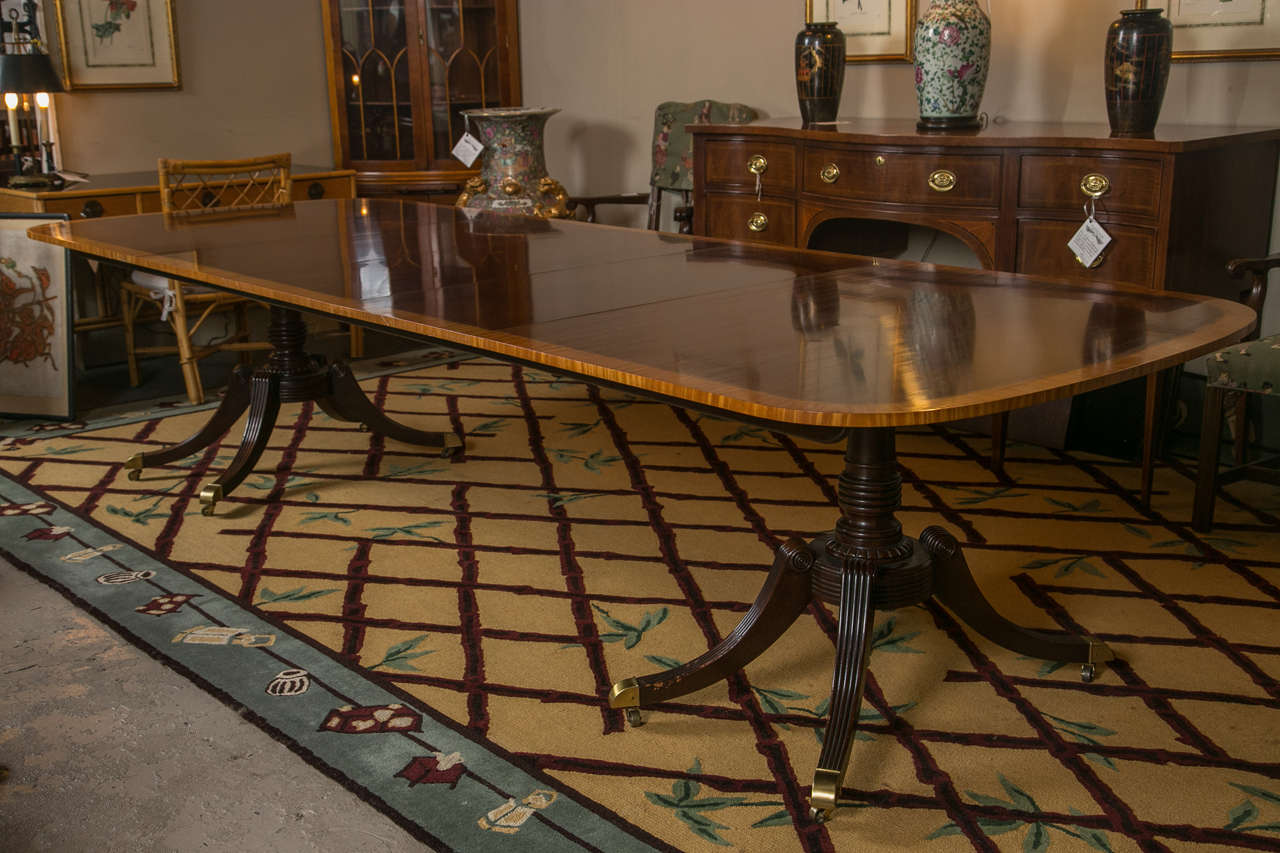 A fine Baker collector's condition satinwood banded double pedestal dining table. This quad legged double pedestal table having brass wheeled casters supporting a wonderful satinwood banded solid mahogany table top. The lower pedestals of oddly