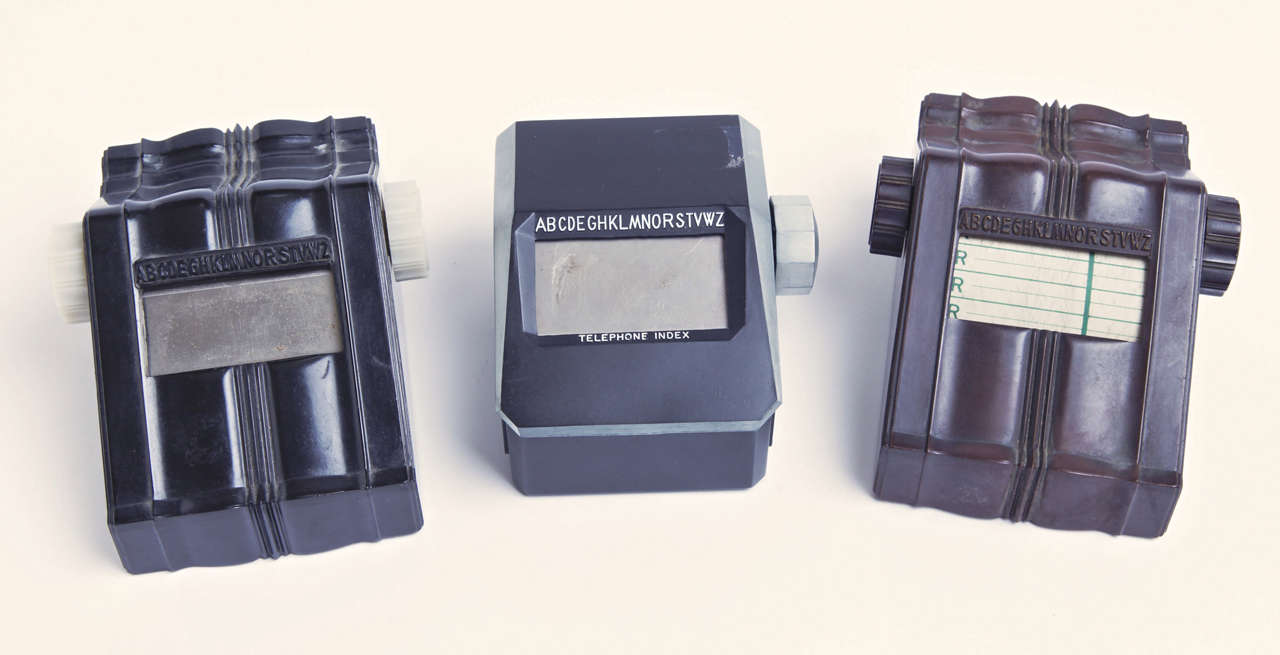 Modelle auf der linken und rechten Seite, beschriftet mit dem offiziellen Design-Logo von Bel Geddes.
Ein patentiertes Gehäusedesign von Bel Geddes.
Links ist schwarzes Bakelit mit weißen Bakelitknöpfen.  Fehlende Indexrolle.
Rechts ganz aus