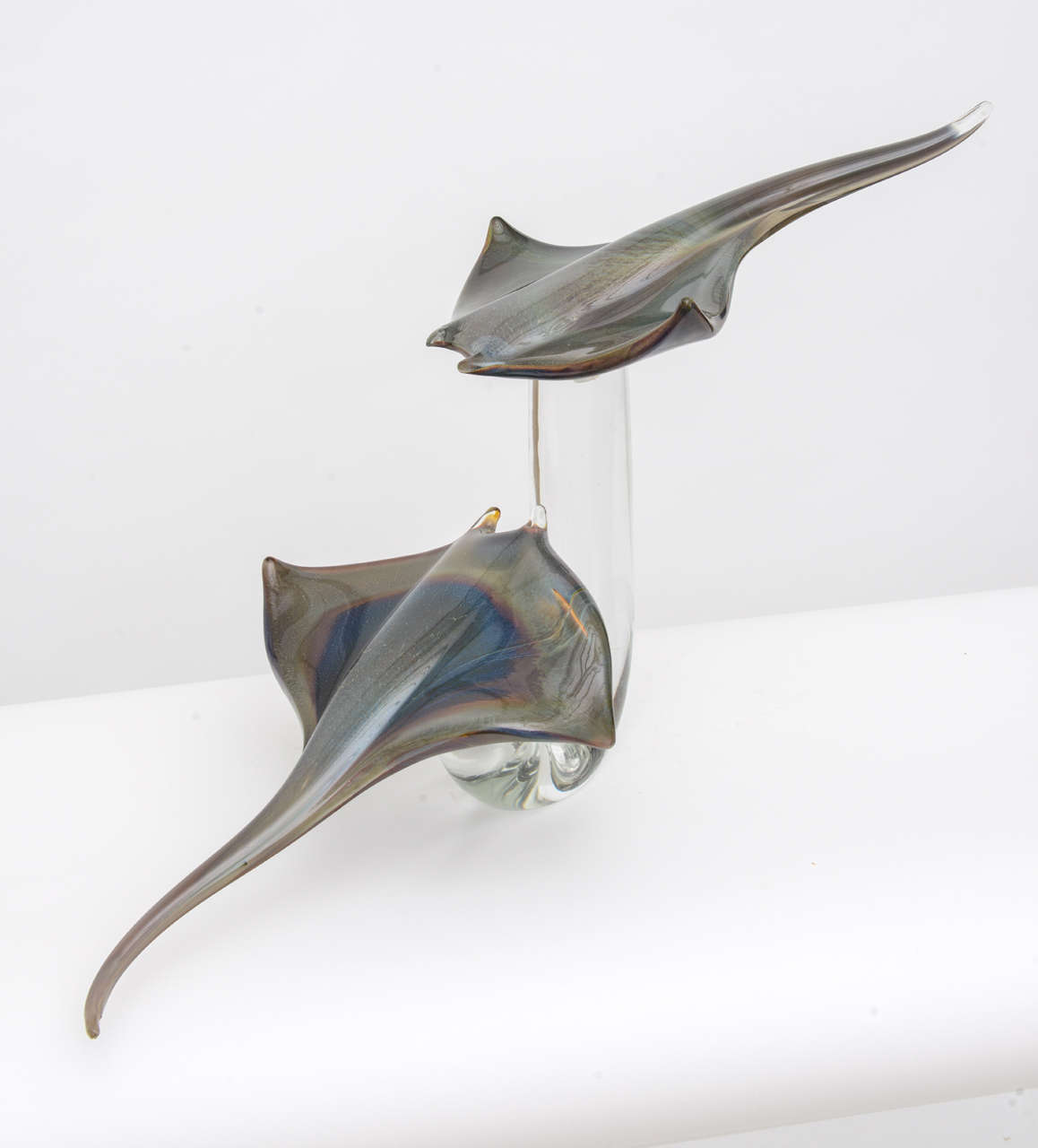 Handblown in Murano, Italy, using the massello technique, this exceptional sculpture consists of two handblown glass fish mounted on a solid tubular curved crystal base. The coloration of the rays varies fantastically from blues to greens with golds