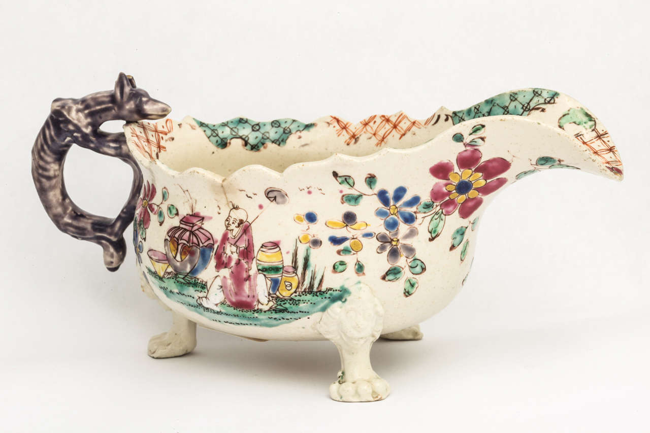 A rare and fine English saltglazed stoneware footed sauceboat, the sauceboat with skeletal fox handle, three lion's head and paw feet, decorated with Oriental figures and flowers