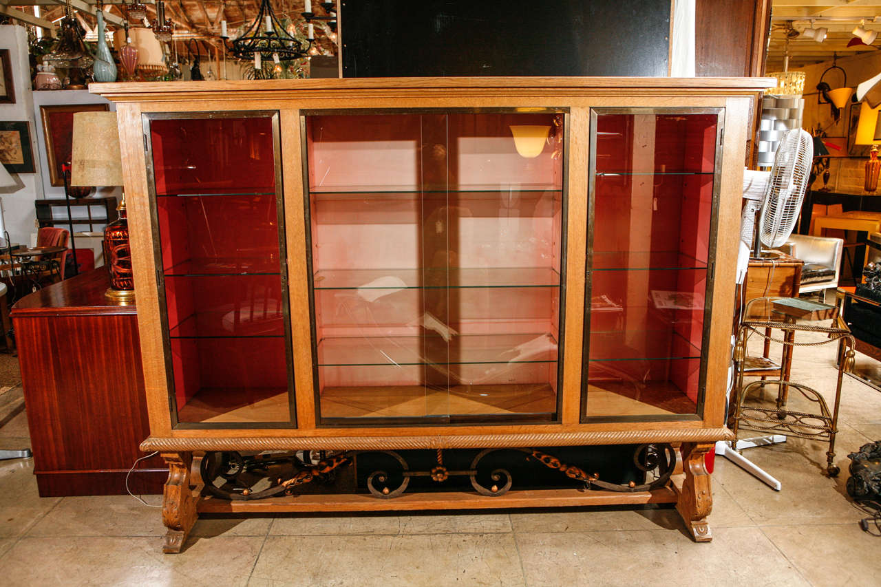 An impressive French Modern display cabinet. Made of oak with brass door frames. Base is decorated with a gilded wrought iron stretcher. There are three display sections with three glass shelves each. Side display cases have locks and keys. Top has