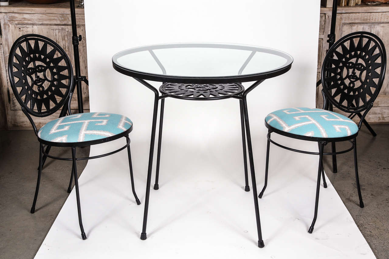 Mid Century iron bistro set with sun face motif. Has a glass top table and two newly upholstered chairs in sunbrella fabric.