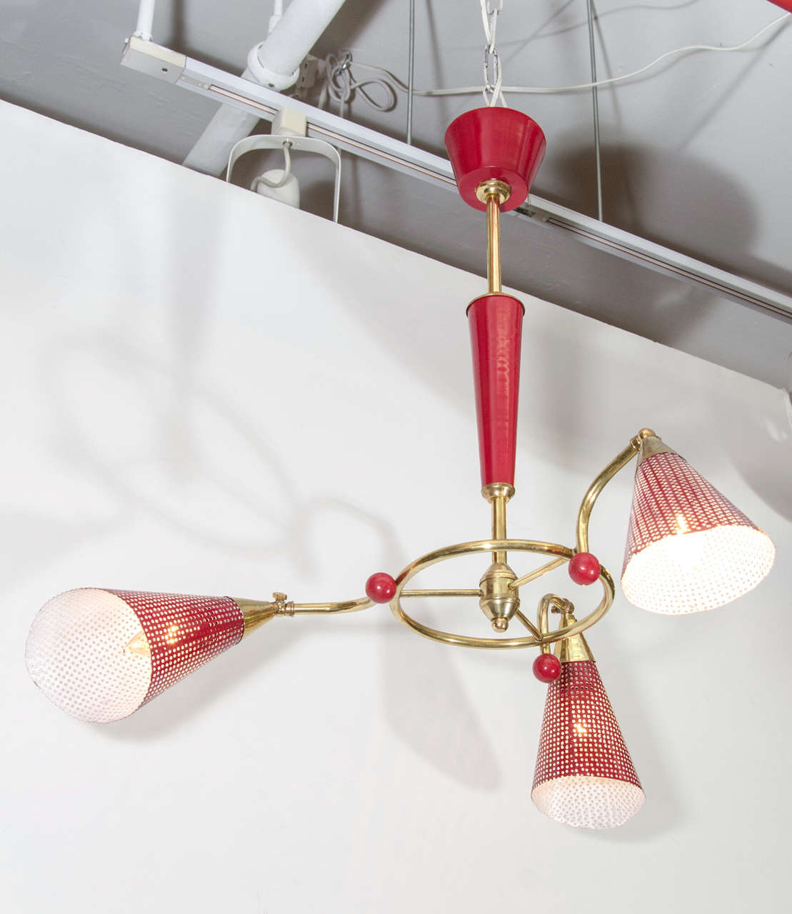 An Italian vintage three-arm chandelier, circa 1960s, with red enameled perforated metal shades (white interior), on curved arms with red ball detail, affixed to a brass frame, suspended from a tapered bright red canopy. Good vintage condition, with