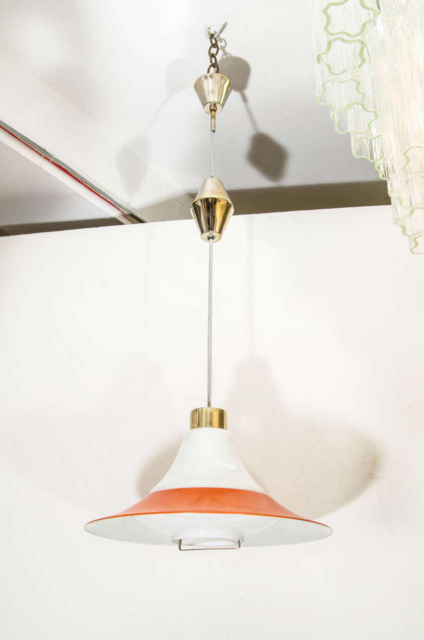 A vintage space age Mid Century pendant light with a white and orange enameled metal shade with brass cap and rod.