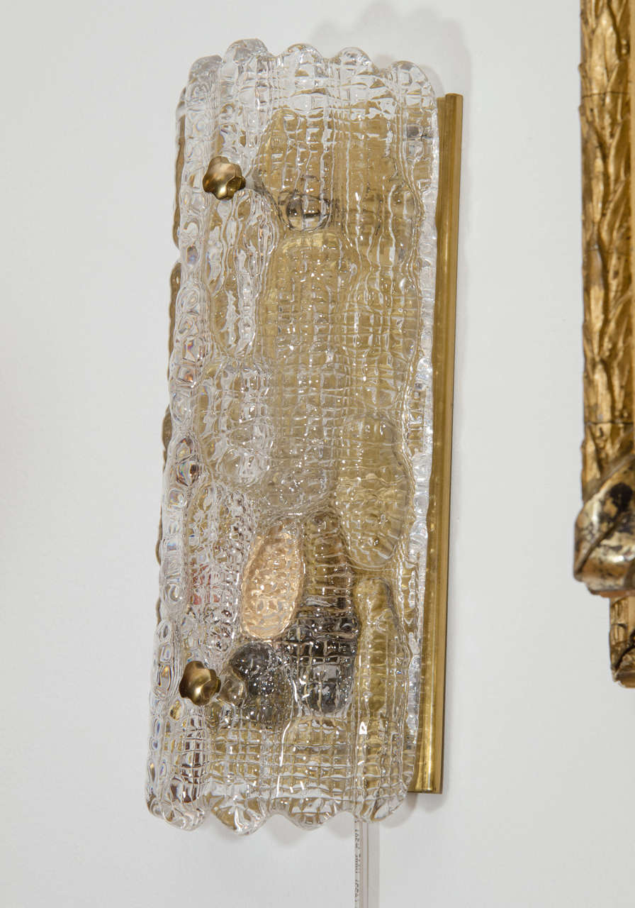 Des appliques en verre moulé et sculpté encadrent un cadre en laiton étincelant. La plaque arrière en laiton diffuse une lumière confortable et dorée à travers le verre moulé transparent. Avec deux ampoules de 60 watts chacune, cet ensemble brille