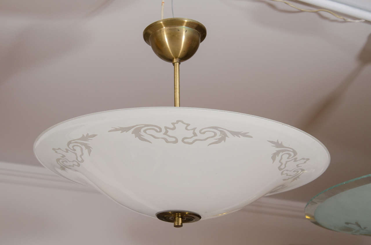 Whimsically etched with stylized leaf motifs, the lacy, frosted white glass is supported by a brass disc and finial on a brass stem.
