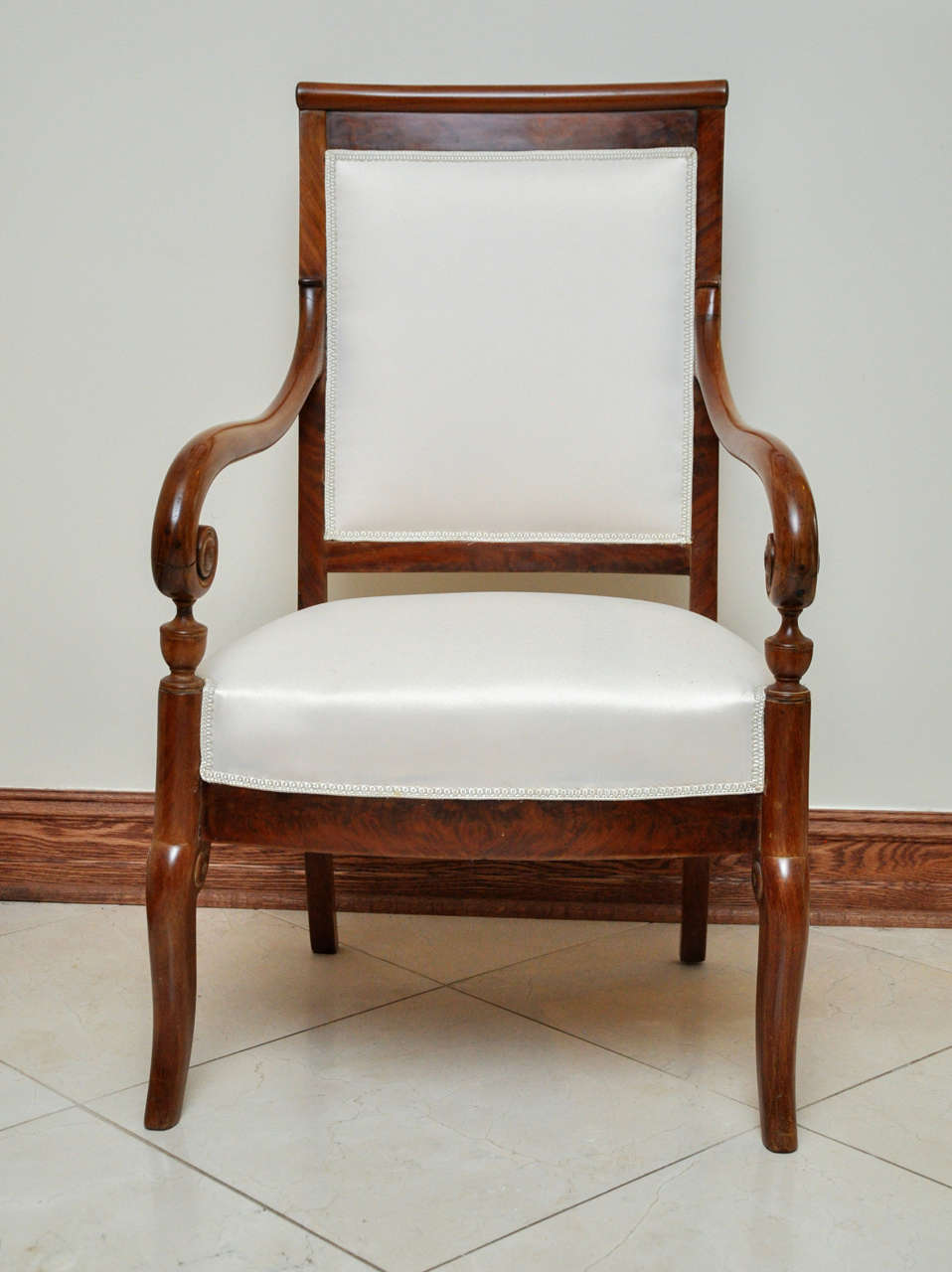 This elegant mahogany armchair is distinguished by its curved, overscroll crest rail at the top of the high backrest. Also striking are the graceful arms which flow into detailed scrolls surmounting small urn-like supports. Simplified 