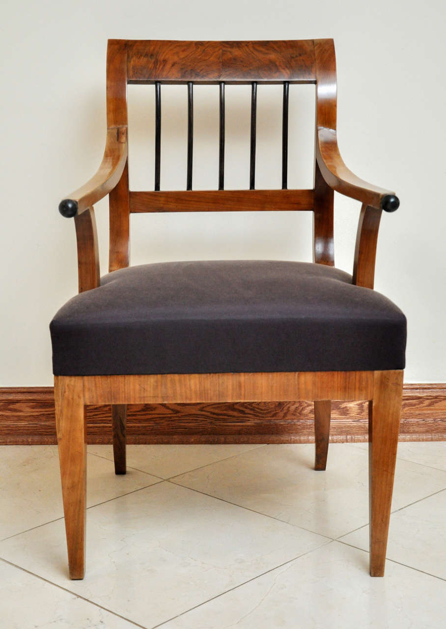 This stately chair is dominated by an elongated S-shaped back with similarly curved cylindrical, ebonized slats, which provide a bold contrast to the rich, well-figured veneer. The curved back is echoed by the long, sinuous arms with spherical