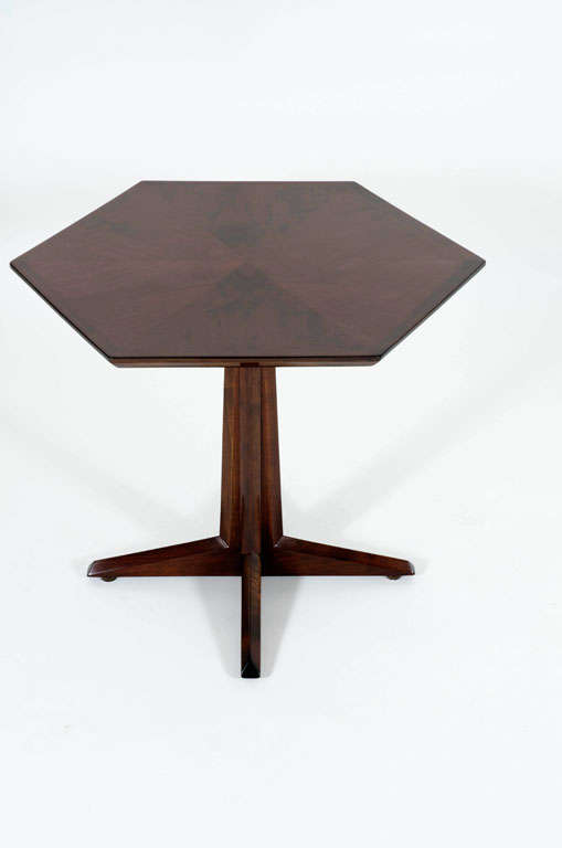 A wonderful occasional table comprising a hexagonal top with six walnut wedges in a bookmatch pattern and a walnut trim supported on a pedestal base comprised of four pieces that terminate in long tapered feet. By Drexel. U.S.A., circa 1950.