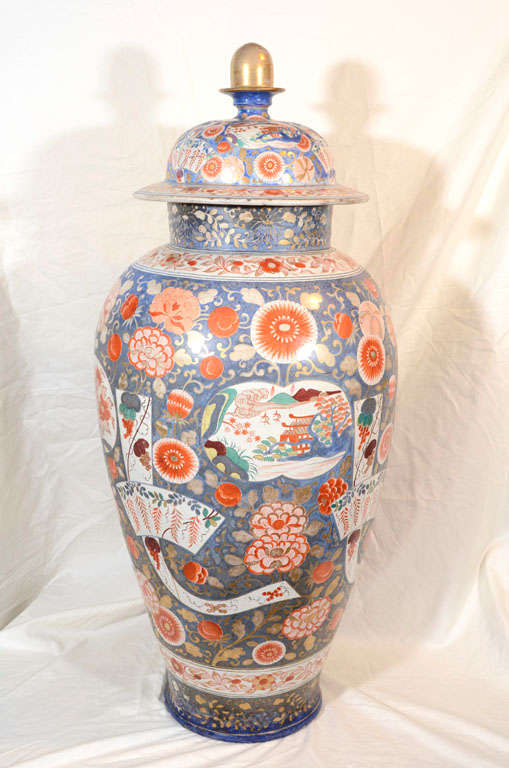 A pair of French faience, Imari, covered vases with a blue ground fully decorated with an oriental theme of flowers, fantastic beasts, and scenes of mountains and far away pavillions.