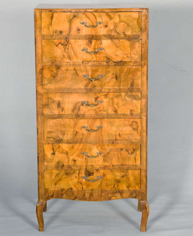 Lingerie chest, veneered in olivewood patchwork burl, having slight serpentine front, seven drawers with brass pulls; raised on square section cabriole legs.

(Keywords: Highboy, commode,