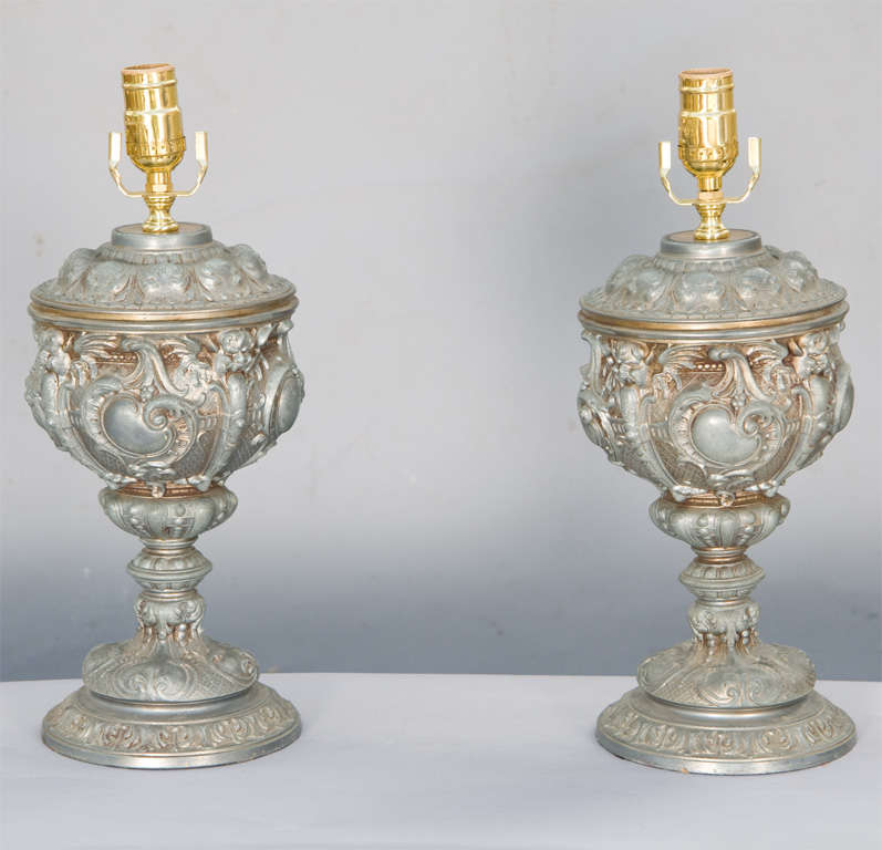 Paar Lampen aus Zinnguss, jeweils eine gut gegliederte Form einer Urne mit Deckel, beleuchtet.