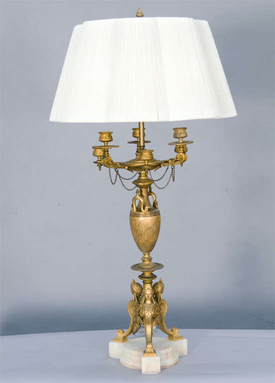 Pair of lamps, of grand scale, each a fine example of Egyptian Revival gilt bronze candelabra,  having six candlepots joined by chain swags, over vase etched with classical motifs, raised on a trio of herms, mounted on tripartite base of onyx. Shown