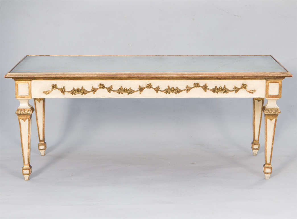 Coffee table, painted and parcel-gilt, having mirrored top inset in molded frame, apron with gilded swag details, raised on square tapering legs.