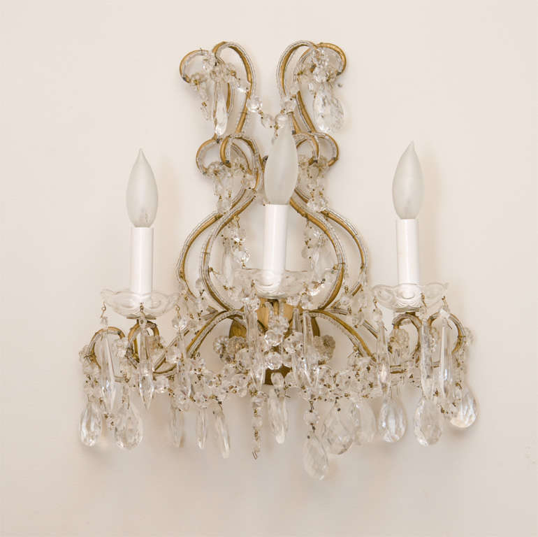 Pair of sconces, in Maria Theresa style, each having a frame of beaded gilded iron, three scrolling candlearms adorned with beading, terminating in scalloped glass bobeches, the entire fixture draped in swags of crystal strands, prisms and teardrops.