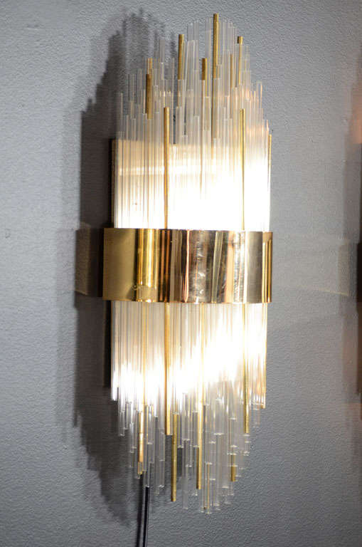 Outstanding modernist sconce comprised of glass rods and
gold-plated rods in alternating heights, creating multiple tiers. Wall sconce has a sculptural design with Art Deco skyscraper elements. The sconce has a large brass center banded detail as