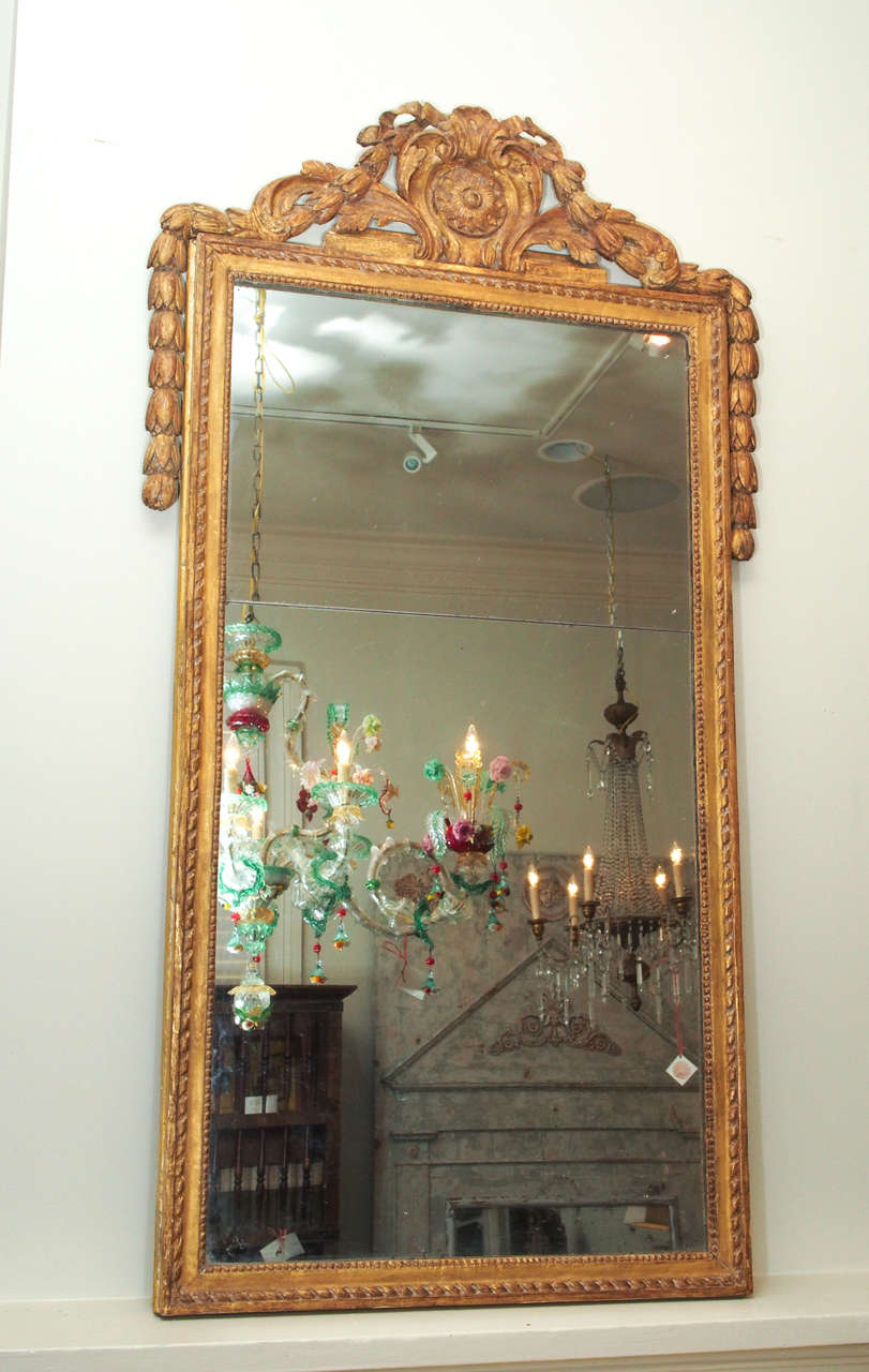 A tall gilt wood mirror in the neo-classical taste, the frame flanked with a thick and beautifully carved bell flower rope, the cartouche with a deeply sculpted rosette patera.