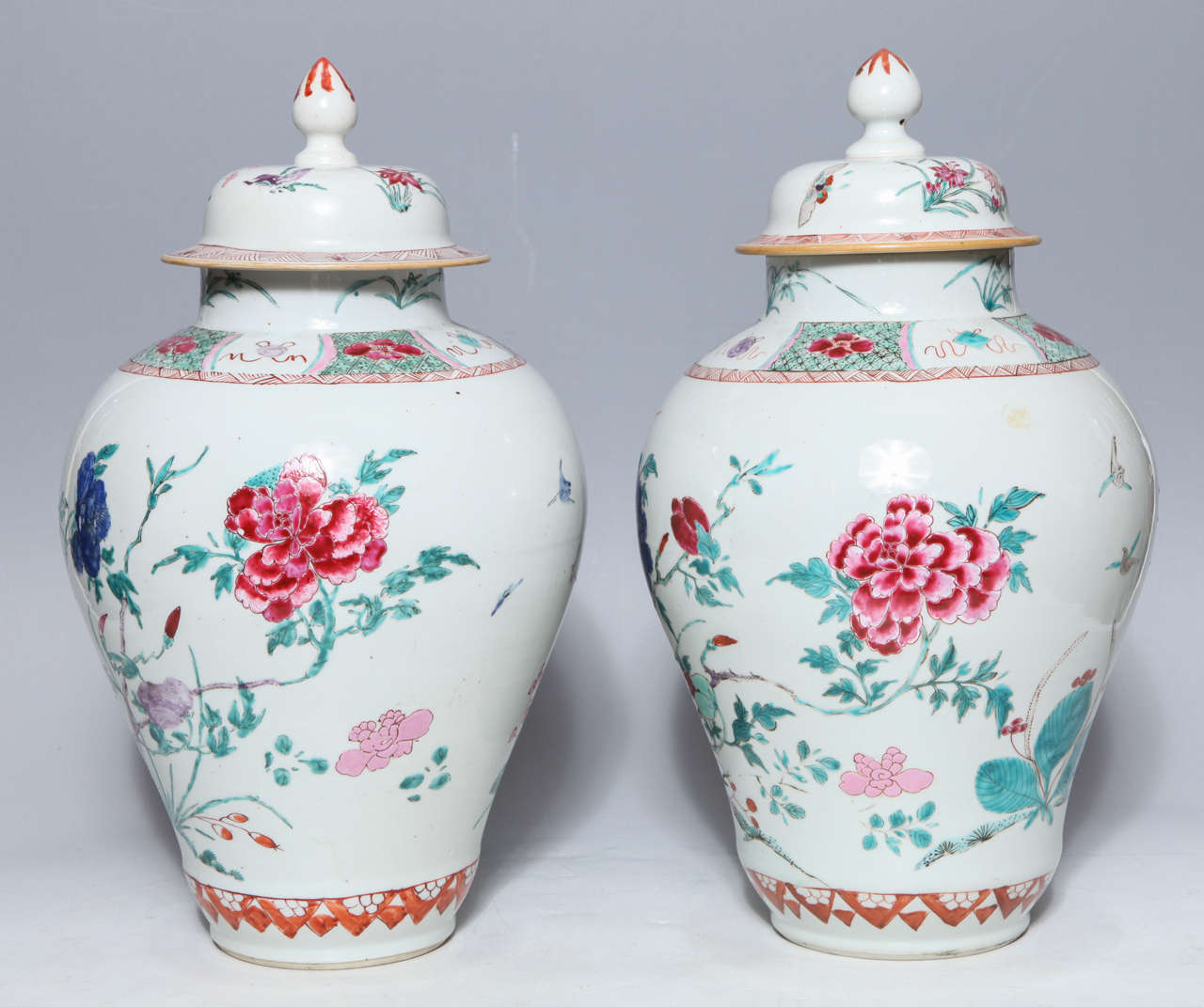 Pair of 18th century Chinese export Famille Rose porcelain covered jars. Spring flowers sprout from jagged rocks while exotic birds peer over the lush garden. There are delicately enameled ribbon-tied precious objects at the shoulder of the jars.