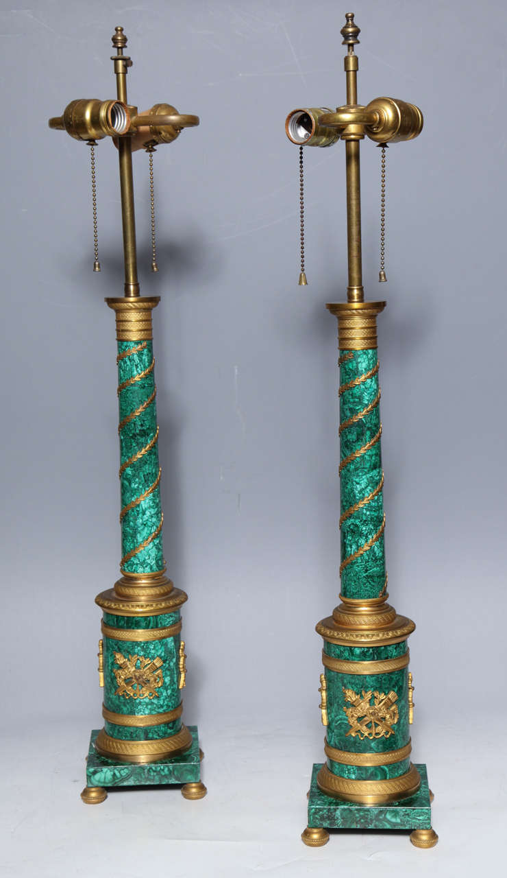 Pair of Russian neoclassical malachite and gilt bronze column table lamps. The bronze detailing glows against the striking dynamic green of the malachite.

Dimensions: 
Height with electric 28