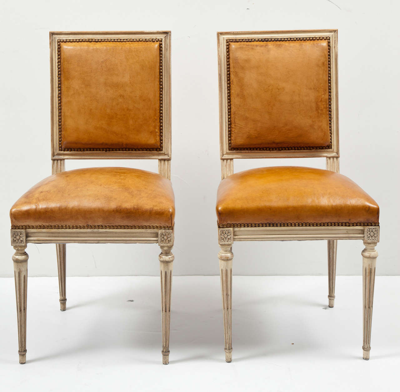 A set of six painted dining chairs in the elegant, understated style of the Louis XVI period. These chairs are newly re-upholstered in a rich, cognac color leather with brass nail heads. With their clean lines, they can be a wonderful additional to