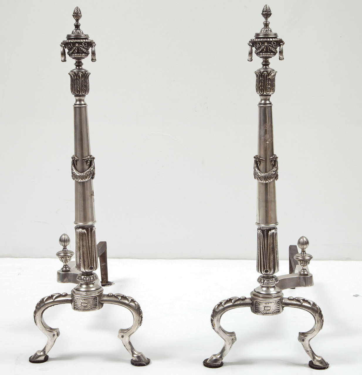 A striking pair of silver plate andirons with beautiful and intricate neoclassical details.