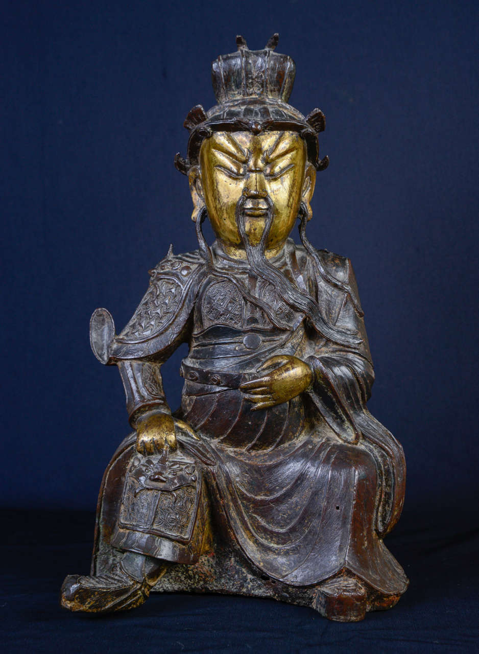 A bronze figure of seated Guandi wearing an elaborate armour, including breast plate secured with a belt, his face with severe expression, moustache and long beard, elongated earlobes and topped by a specific bonnet.
China Ming Dynasty, 17th