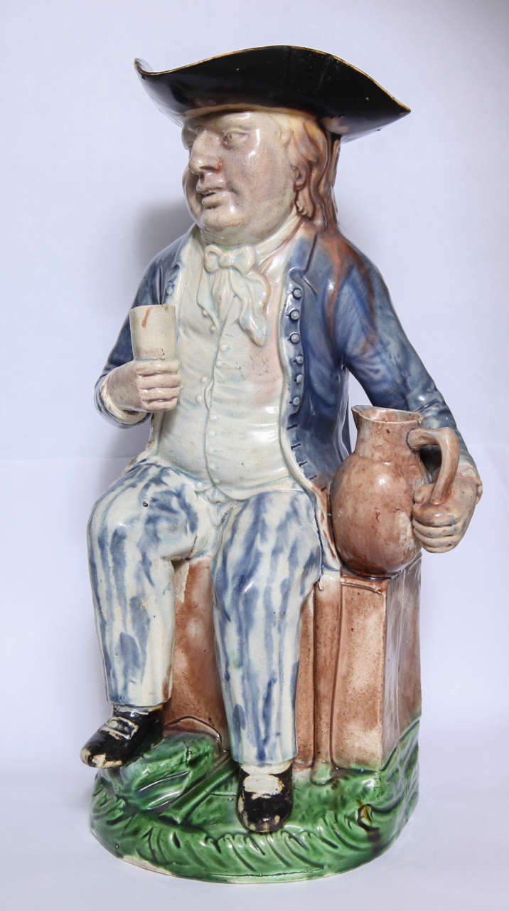 A rare Ralph Wood Sr. Planter toby jug, the man seated on a chest and holding a pitcher in one hand and a beaker in the other, decorated in translucent glazes of green, blue and brown