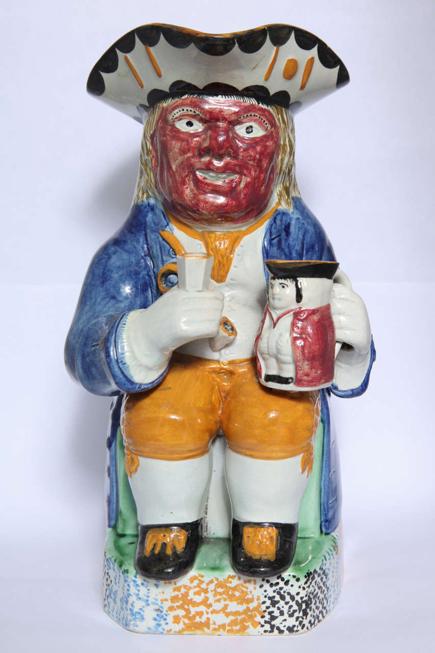 A rare English pearlware pottery toby jug, the red faced seated man holding a smaller toby jug and beaker, a pipe on his vest, figural handle, decorated in underglaze Pratt colors