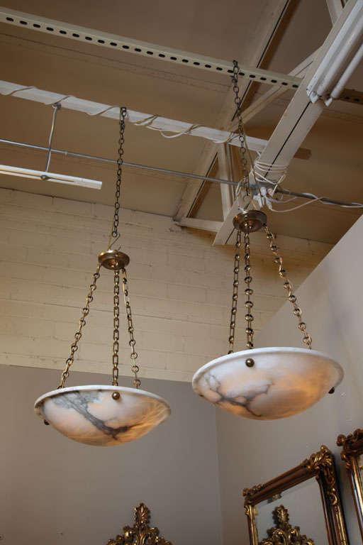 Elegant pair of French alabaster pendant lights with bronze fittings in the Directoire style. Interior lighting has been refitted to keep light bulbs away from alabaster and provide a more even light distribution. Uses 3-40 watt max candelabra base