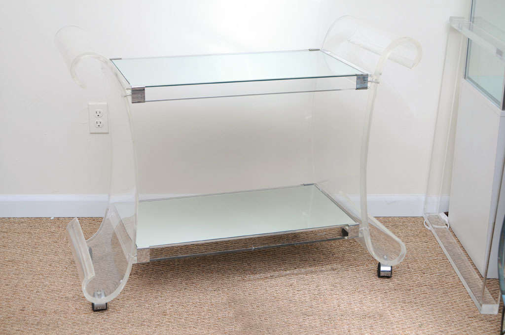 Chic retro modern bar cart, sculpted in lucite with a multi level shelving in mirror. The bar cart is on casters so it does roll for easy mobility.