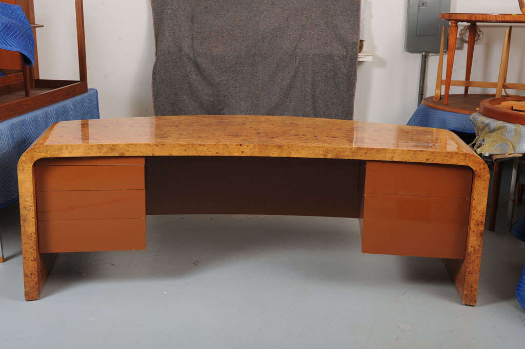 Vladimir Kagan Designs, Inc. A large curved desk with a maple-burl top and laquered wood drawers.<br />
Desk features five drawers and one pull-out surface. Signed with decal manufacturer’s label to drawer: [Hand Made in The Workshops of Vladimir