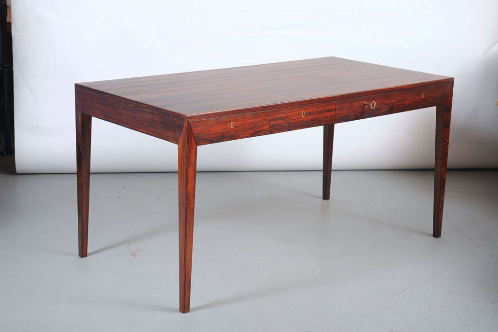 Rosewood writing desk with tapered legs, includes four drawers with brass keyholes and one key.