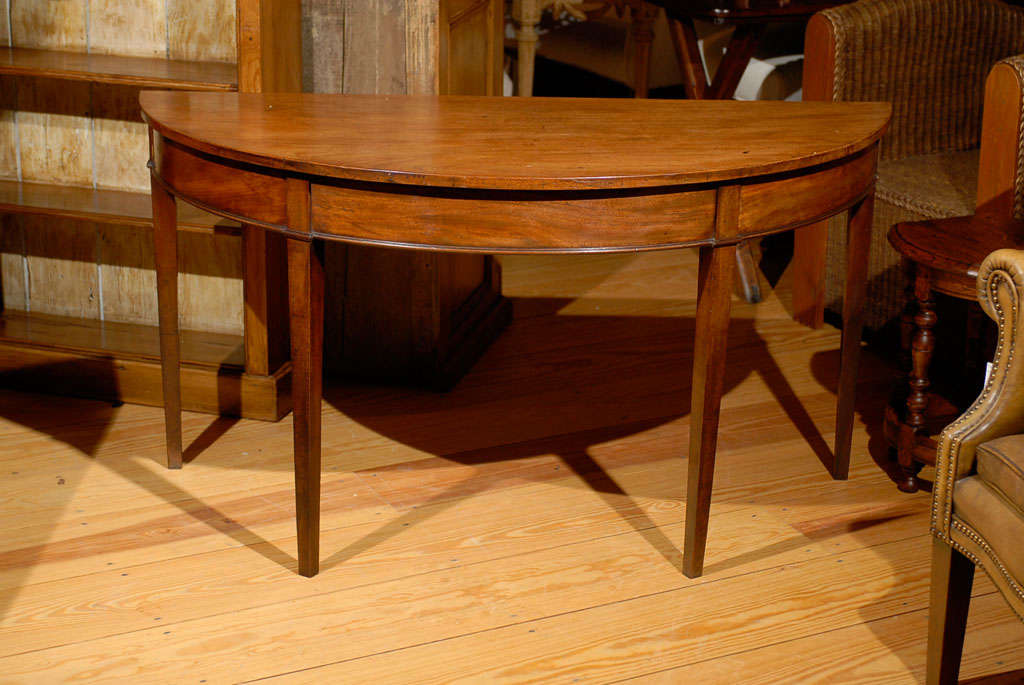 This pair of elegant English 19th century Hepplewhite style mahogany demilune tables features semi-circular tops over sober aprons resting on four square, tapered legs, providing great stability. These freestanding demilunes are typical of the