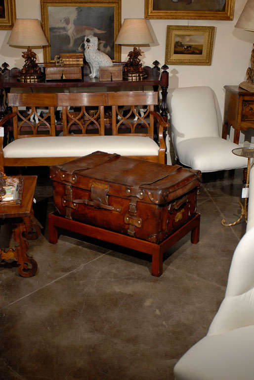 An English leather trunk on custom stand made into a coffee table. This English trunk on stand from circa 1880 features a leather travelling case with lateral handles and leather straps raised on a custom rectangular mahogany stand. This well-worn