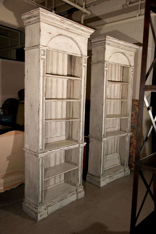 Pair of tall Swedish style bookcases, 20th century, distress painted in off-white, each has shelving and open front, flanked by columnar uprights leading to domed decorative tops.
