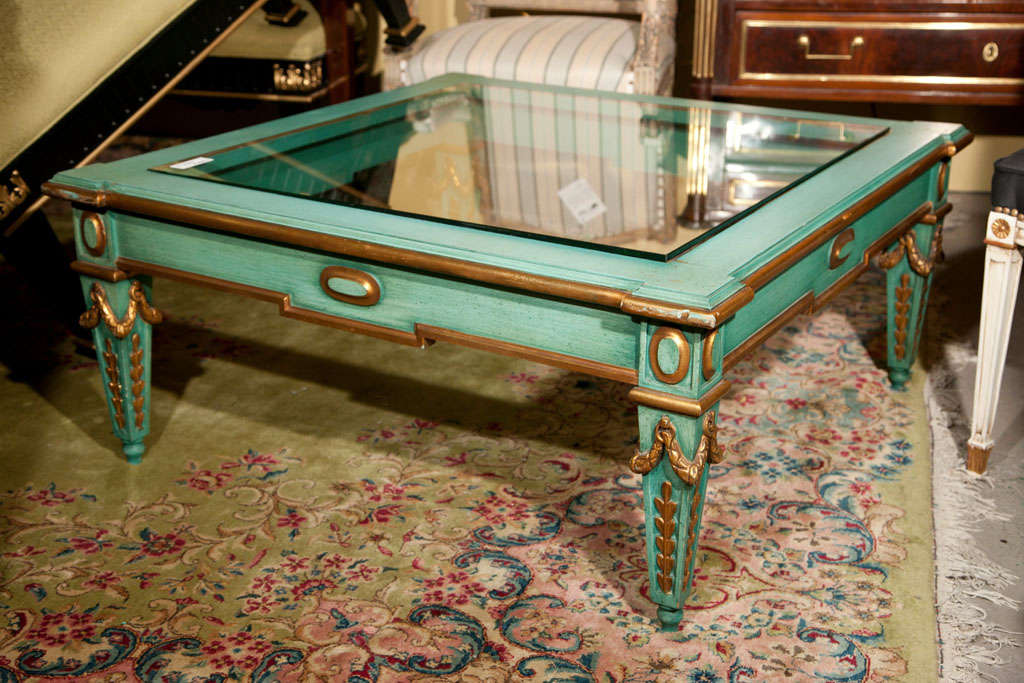 French Empire style square coffee table, circa 1940s, overall distress painted in aqua blue and parcel-gilt, square glass top, raised on squared tapering legs decorated with wreath carving. Attributed to Maison Jansen.