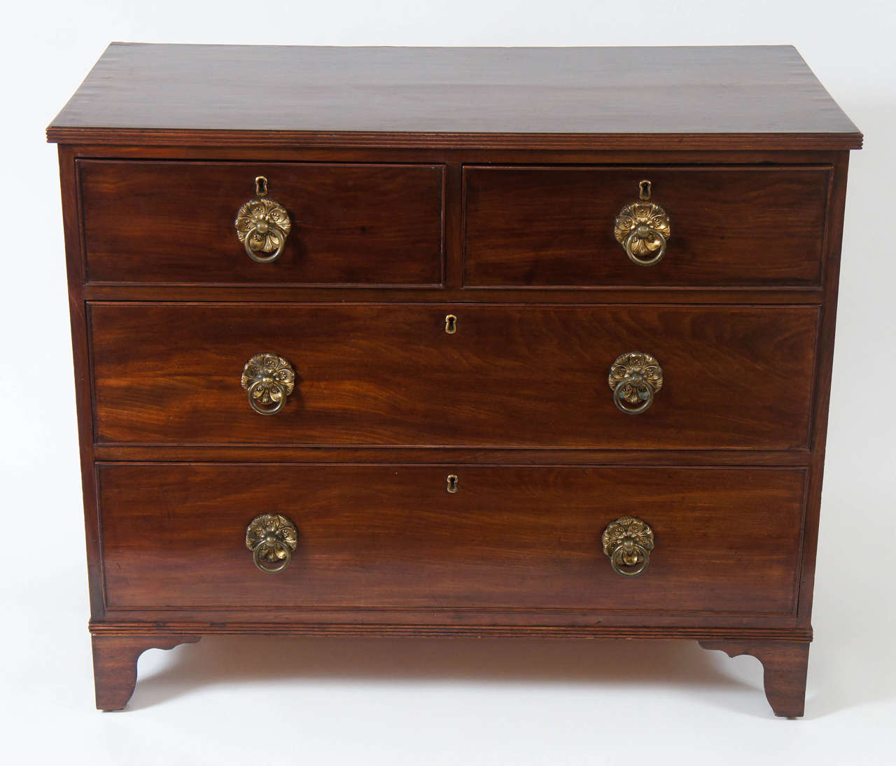 Elegant and refined English Regency period and style mahogany chest of four drawers having reeded edge-band trim on top and base with drawers having original large gilt metal foliate form ring pull hardware.