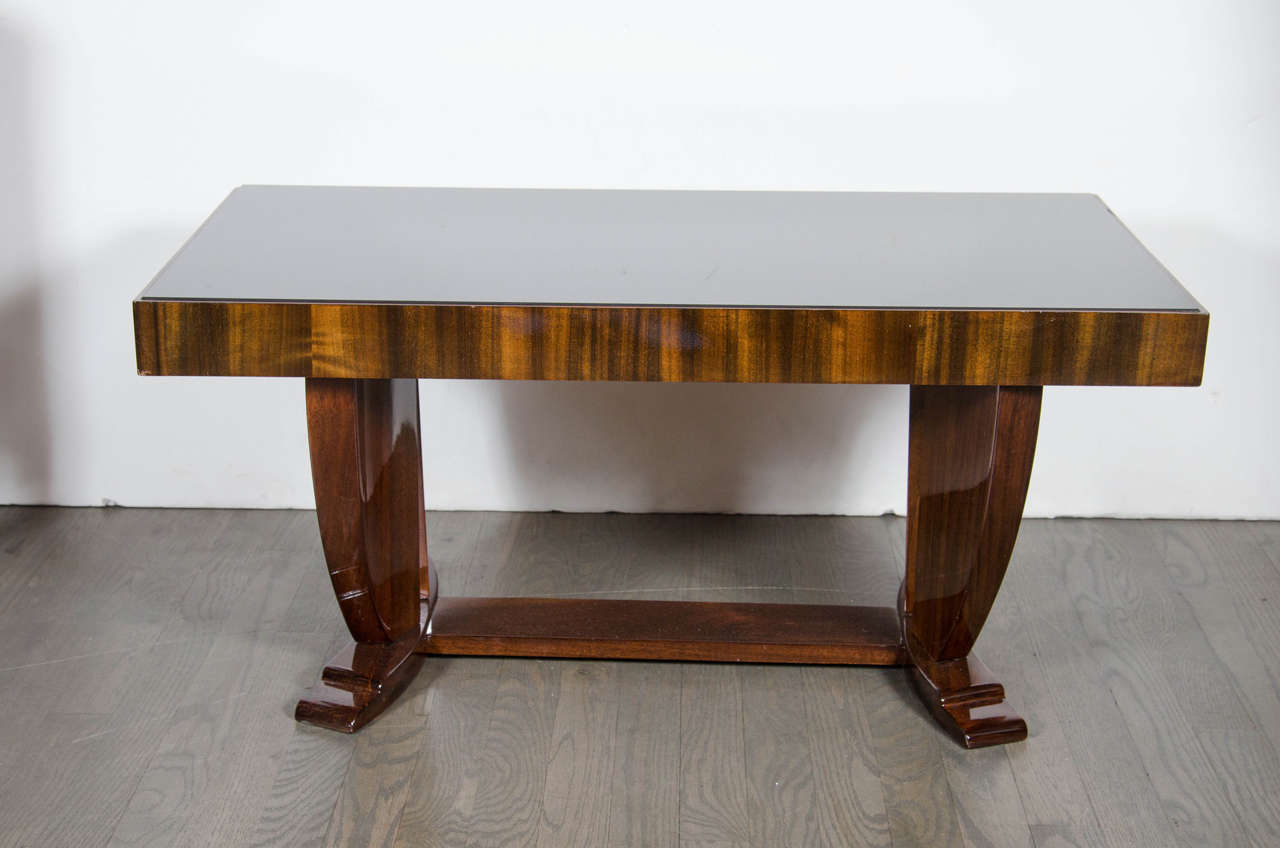 Art Deco Skyscraper style cocktail table in book-matched Walnut with a vitrolite top that has a book-matched Walnut banded surround that sits atop support legs with curved, skyscraper design and arched, stepped feet. The support legs sit at a slight