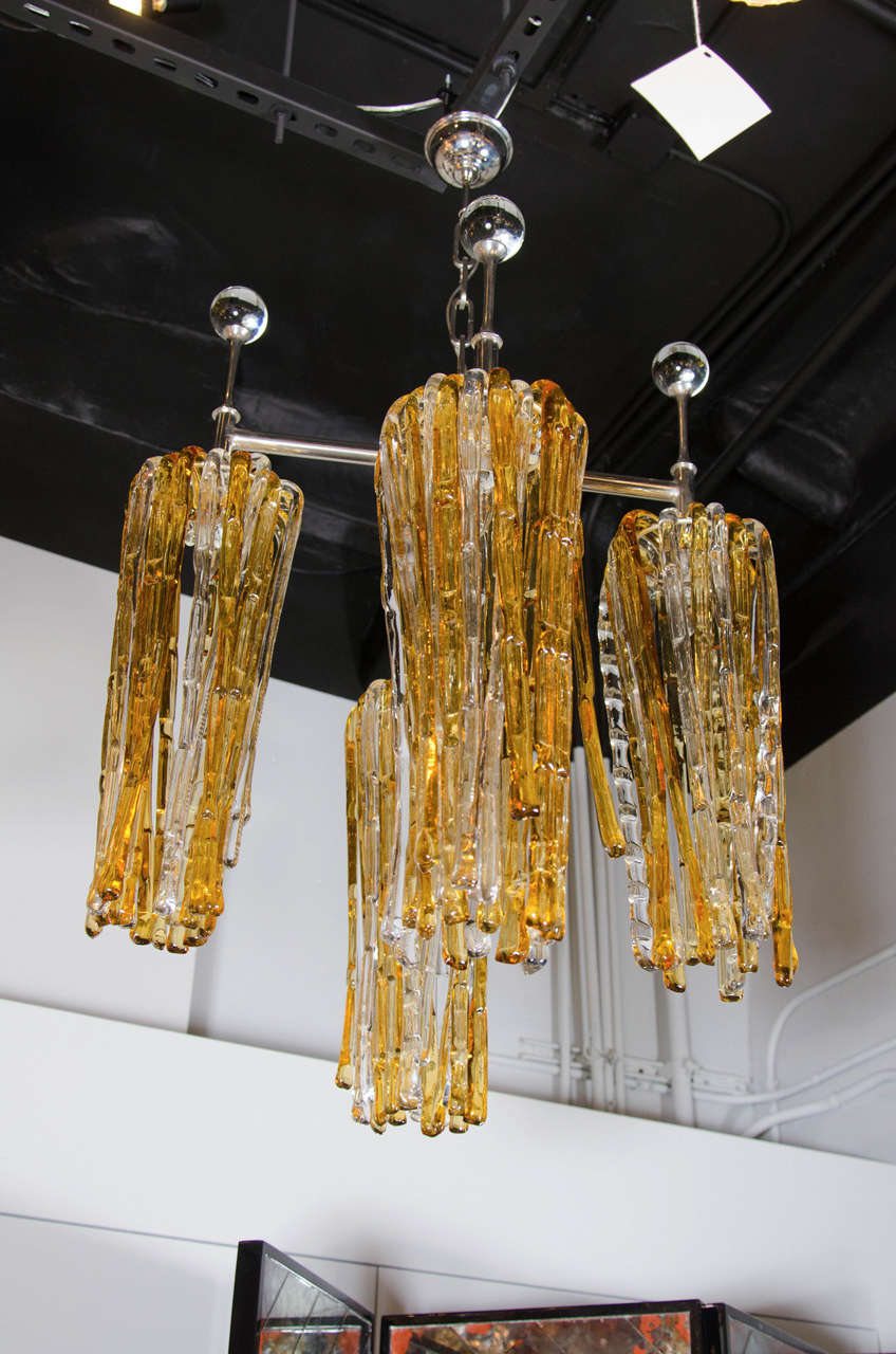 Ultra Chic Mid-Century Modern handblown Murano glass chandelier that features a polished nickel X-form frame with glass ball detailing atop each one of the four arms that supports an array of amber and clear cane shaped Murano glass rods.  Each rod