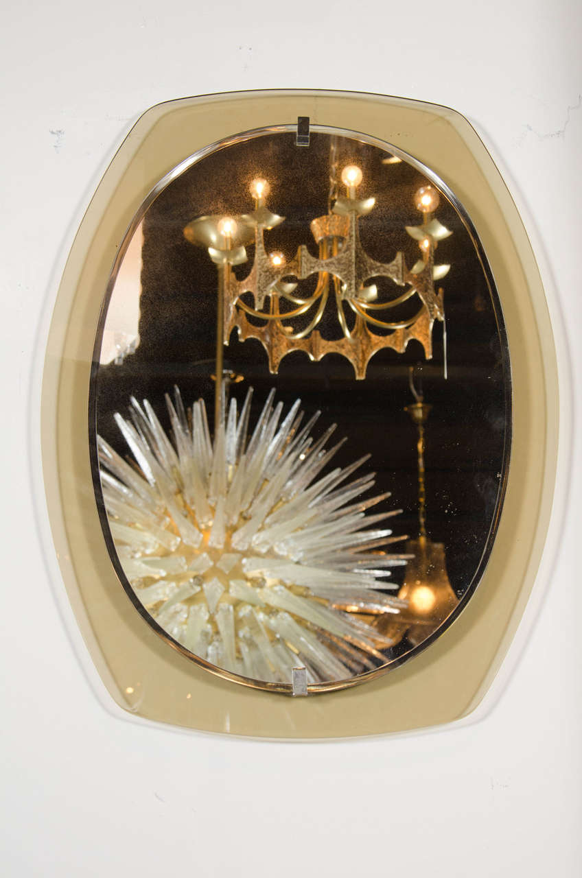 This exceptional Mid-Century Modern mirror by Fontana Arte consists of an oval-shaped mirror surrounded by a border of smoked glass which emulates the form of the mirror but at the same time gives it some shape. This mirror is perfect for a powder