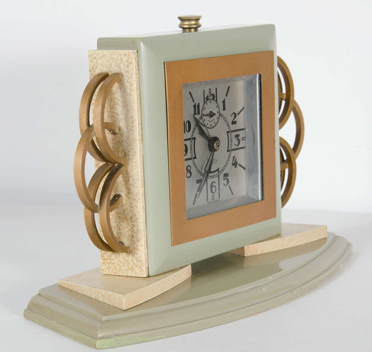 This stunning clock clock features a celadon lacquered base frame and base with gilt concentric ring detailing on the sides and creme accents. Stylized Art Deco numbers and hands in black on a silvered face. The clock has been fitted with a battery