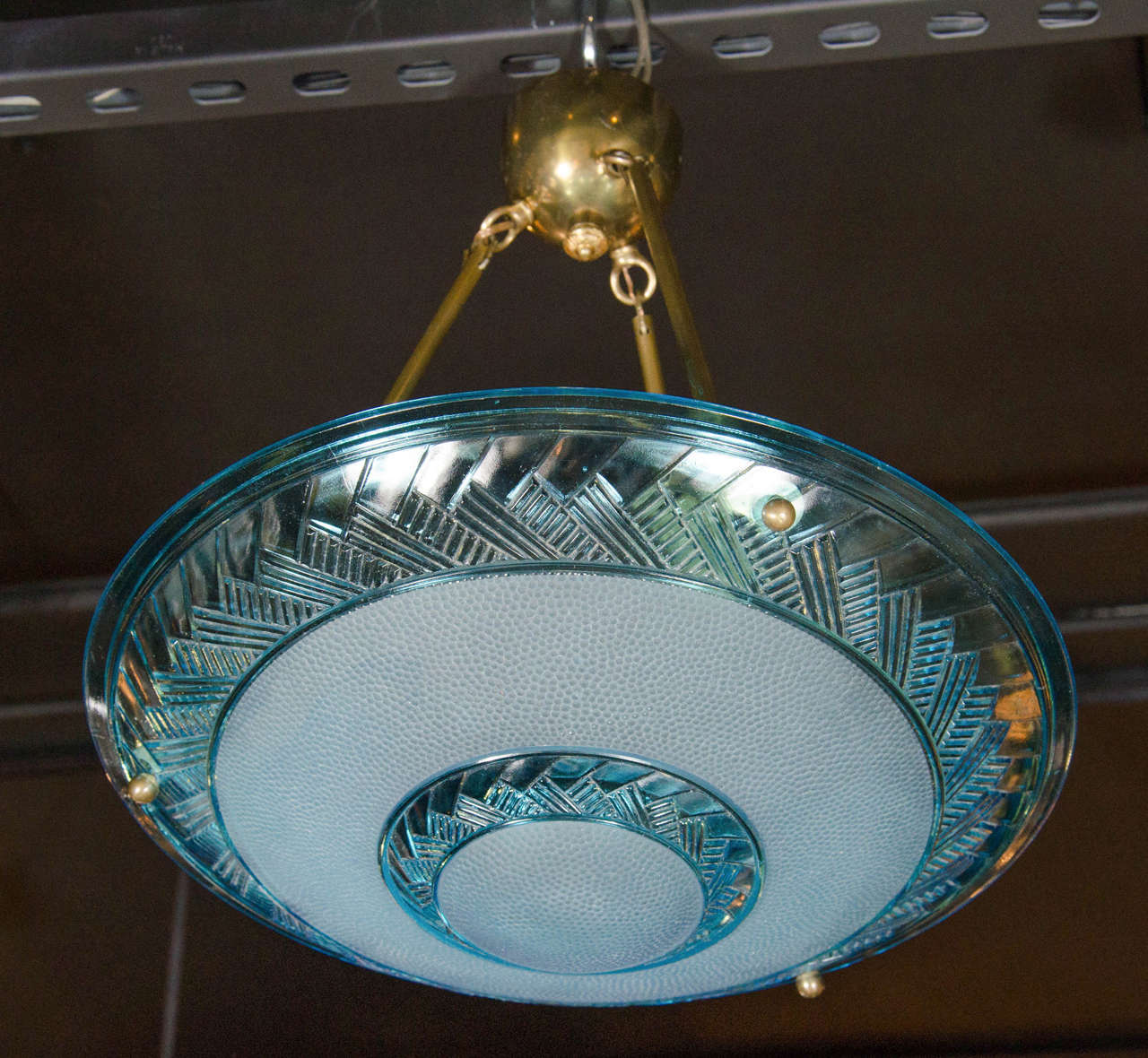 Art Deco flush mount chandelier by Degue with a blue glass inverted dome supported by antique brass fittings and three lights. This flush mount chandelier features two concentric stylized herring bone pattern bands against a pebble textured