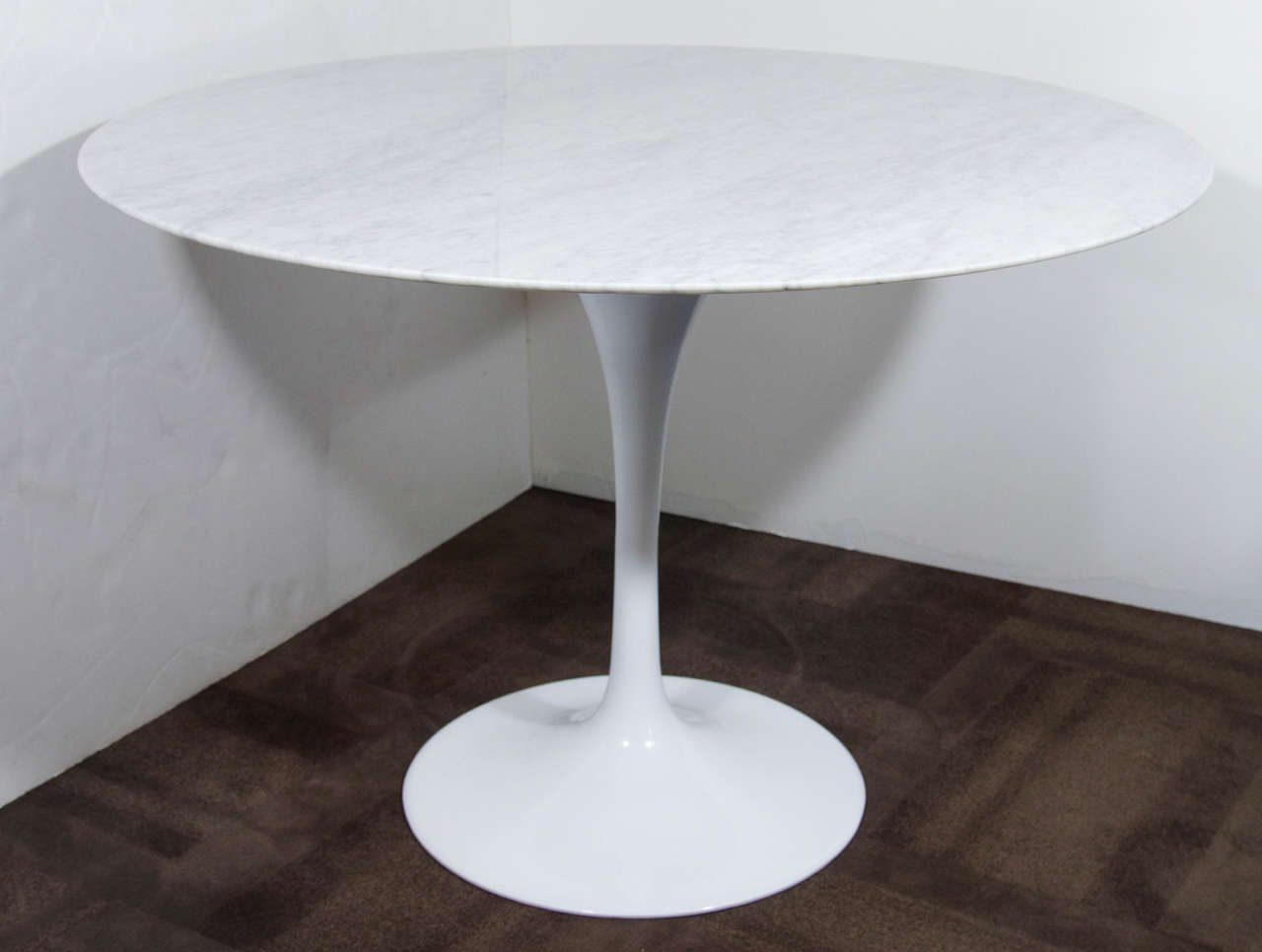 The iconic tulip dining table comprised of solid arabescato carrara marble top over a a stylized cast metal base in a white gloss enamel finish. Round polished white marble with subtle streaks of pale grey. Excellent scale for eat in kitchens,