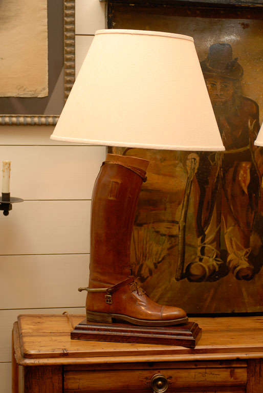 This is a pair of English vintage handmade antique brown leather riding boots with their wooden boot trees, mounted and wired as table lamps with cream-colored Empire shades. The left and right boots each presents a nice warm brown color, laces and
