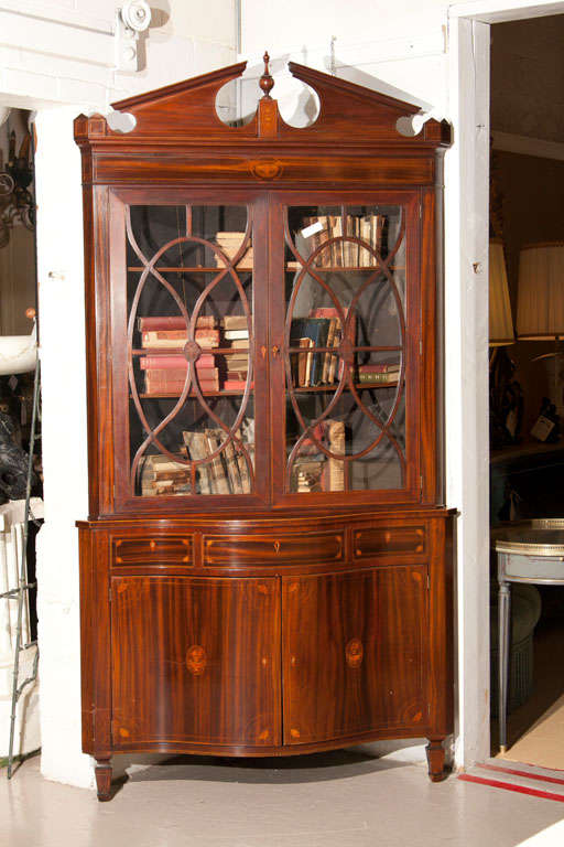A handsome English Georgian corner cupboard, 19th century, the shaped top over a glass two-door cabinet, supported on a conforming case fitted with three narrow drawers over a cabinet, raised on fluted bulbous legs.